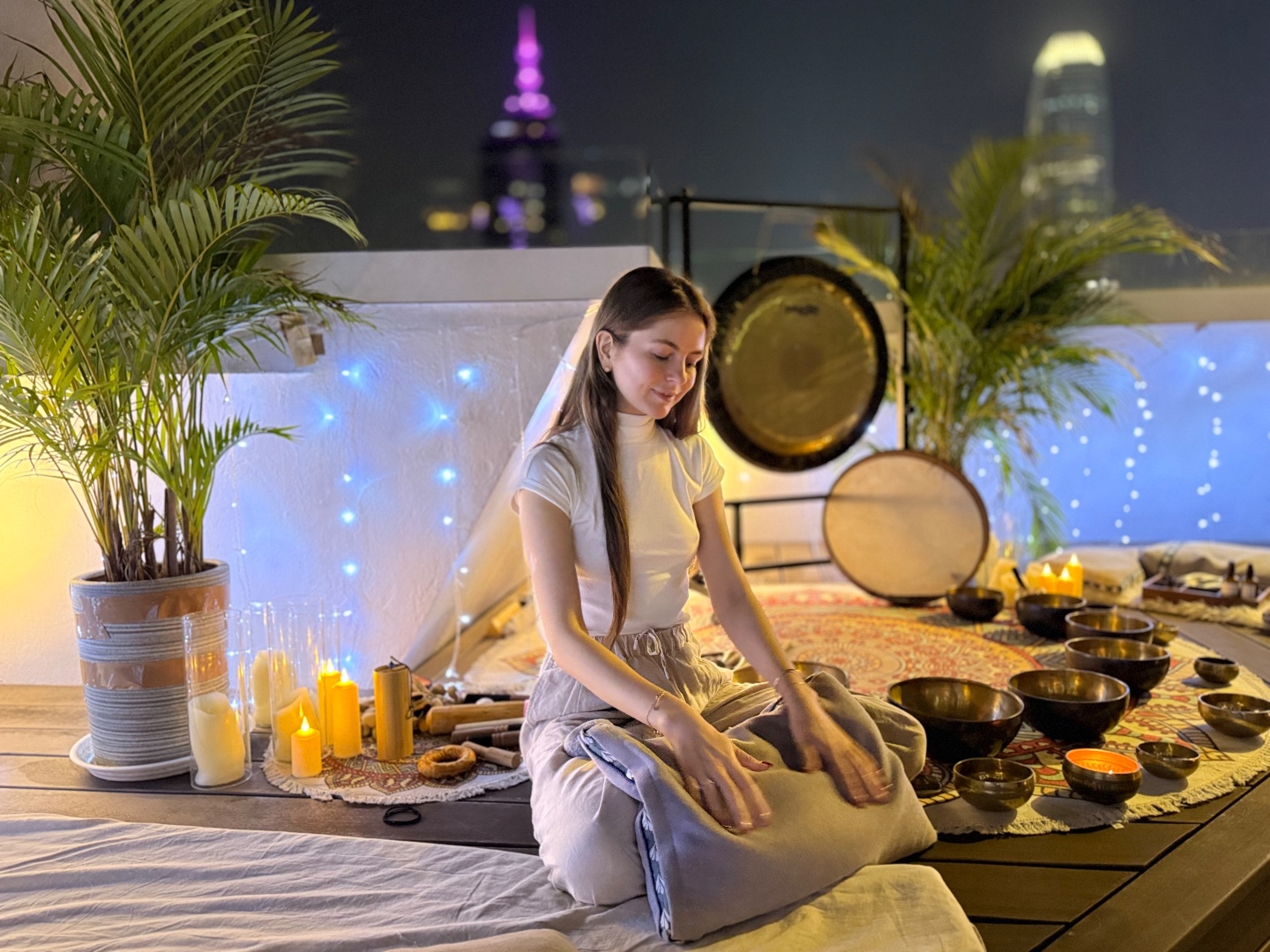 Kate Mormylo seated with Tibetan singing bowls on a rooftop in Hong Kong at night