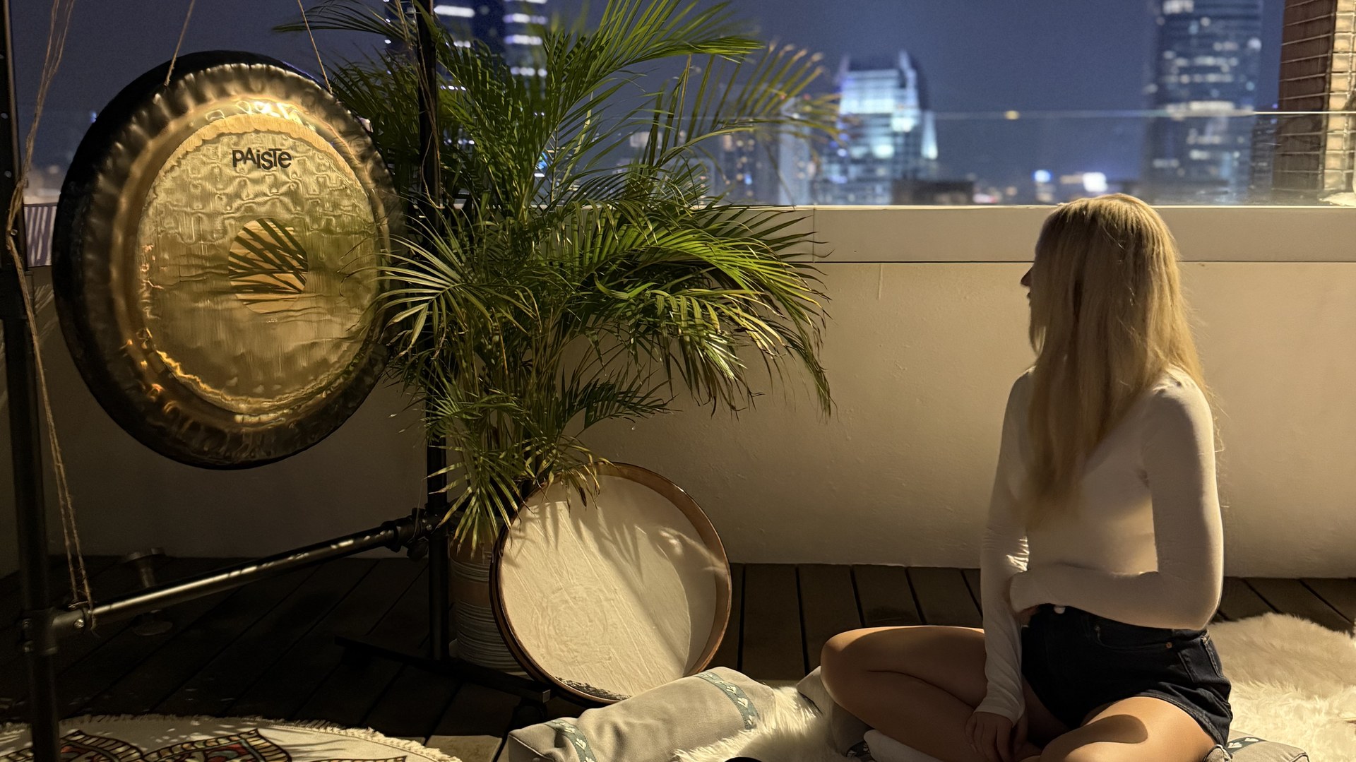 Kate with Tibetan singing bowls and a gong on a rooftop in Hong Kong at night under the open sky